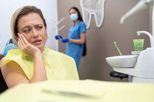 Woman suffering from toothache, sitting in dental chair at the clinic 